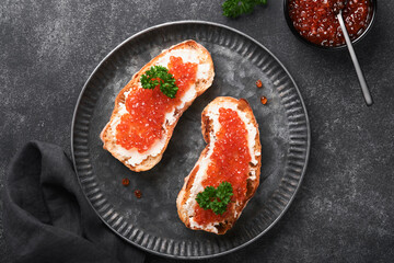 Two sandwiches with red caviar. Salmon red caviar in bowl and sandwiches server on old iron plate on old black table background. Top view. Copy space.