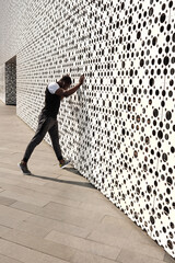 Unrecognizable Black male athlete in sportswear standing against modern building with perforated walls and doing warming up exercises