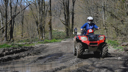 A red quad bike with a girl behind the wheel is about to drive through a puddle in the spring...