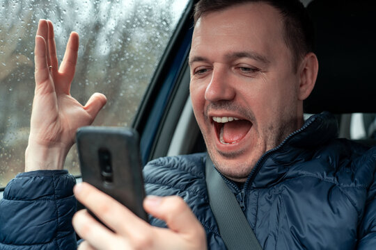 Happy excited millennial man looking at smartphone screen and showing yeah gesture in car
