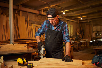 Senior Professional carpenter in uniform sawing wood with an electric jigsaw in the carpentry...
