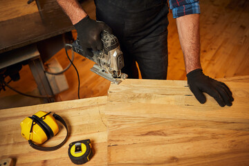 Close up of professional carpenter hands sawing wood with an electric jigsaw in the carpentry workshop