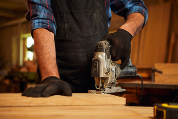 Close up of professional carpenter hands sawing wood with an electric jigsaw in the carpentry...