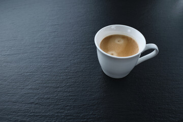 White cup of coffee on a black background. Espresso on black slate.