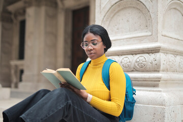 young woman at the entrance of a school reads a book