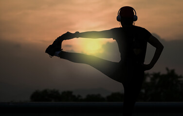 Back view silhouette sporty woman stretching her leg  listen to music from headphone watching sunset, Sport portraits