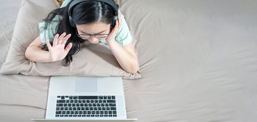 Beautiful Asian woman using zoom meeting and making facetime video, social distancing during covid pandemic period on her bedroom with a pastel green - brown color theme.