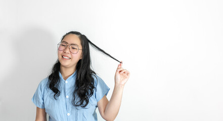 A young asian girl touch her hair smoothly with a big smile on her face. She is wearing a light blue shirt and glasses.