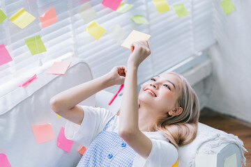 Young Asian girl is writing on sticky notes and pasting them all over the room