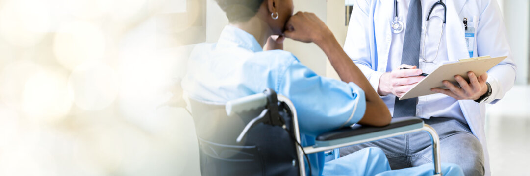 A male doctor takes a male patient who is admitted at the hospital for a walk through the window corridors of the hospital for psychotherapy. by having the patient sit in a wheelchair web banner with 