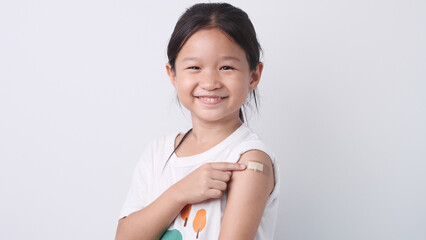 Vaccine concept. Happy Asian little child girl smiling, showing arm with plaster bandage after received, getting COVID-19 vaccine injection. Concept of inoculation, vaccinate, campaign, COVID19, Flu - obrazy, fototapety, plakaty