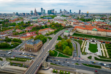 Historyczna panorama miasta z widokiem pod dużym kątem na kolorowe dachy budynków na rynku starego miasta. W tle widok na centrum nowoczesnej Warszawy z sylwetkami drapaczy chmur.