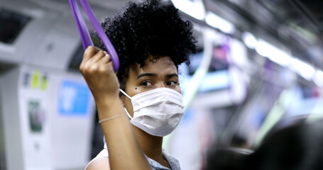African american woman holding subway handrail during pandemic wearing face mask