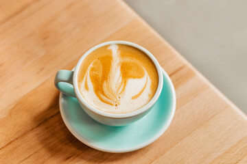 Fragrant and delicious cappuccino with beautiful foam in a blue cup on a wooden table. Beautiful concept coffee on the table. Light design for your coffee shop