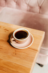 Black strong coffee in a pink ceramic cup on a wooden table. Aromatic freshly brewed Americano for breakfast