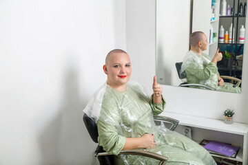 Smiling shaved bald woman with bright make-up in the hairdresser's chair.