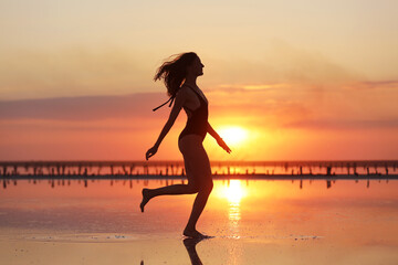 Fototapeta na wymiar silhouette of a young slim woman in a swimsuit who dancing at sunset on the sea. summer holiday