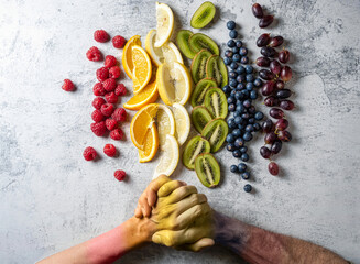 Fruit cut and arranged in the order of the colors of the rainbow. Two hands painted in rainbow...