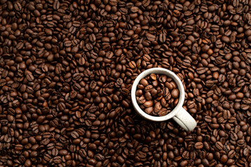 Small coffee cup filled up with roasted coffee beans flat lay view