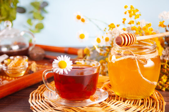 Cup of herbal tea with flowers, honey in jar, teapot and and various dried herbs on the tray.
