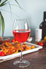 Glass of red wine and food chicken tabaka with vegetables on the baking sheet on the background.