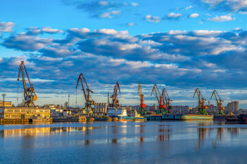 Obraz premium Ships, barges in soft focus in the cargo port against the background of sunset, dawn, in the rays of the sun in Cherepovets, Russia. Industrial urban landscape, transport logistics.