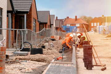 Builders installing paving blocks during road and footpath construction on a semi-dray concrete...
