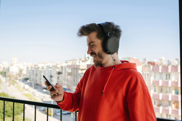 Young happy handsome man wearing red hoodie doing video call using smartphone with headphone. Man watching video on phone or video call or scrolling on social media.