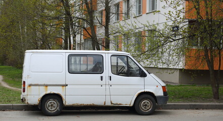 Fototapeta na wymiar An old rusty white minibus parked on the road, Shotman Street, St. Petersburg, Russia, May 2022