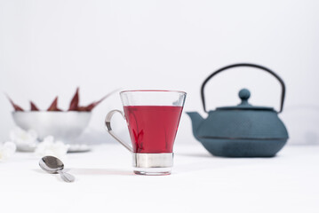 Una taza transparente de té de bayas con tetera de hierro azul sobre una mesa blanca