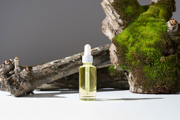 Botella de aceite esencial con cuentagotas sobre un tronco de árbol con musgo. Producto cosmético...