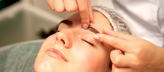 Eyebrow massage. Beautiful caucasian young white woman receiving an eye and eyebrow massage with closed eyes in a spa salon