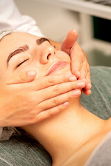 Obraz na płótnie Canvas Beautiful caucasian young woman receiving a facial massage with closed eyes in spa salon, close up. Relaxing treatment concept
