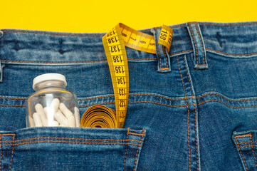 yellow measuring tape and a glass jar with pills are in the back pocket of blue jeans on a yellow background.