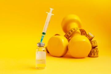 syringe is stuck in jar, dumbbells and a measuring tape are lying next to it on a yellow background, close-up. the concept of doping in sports, steroids, testosterone and other drugs for weight loss.