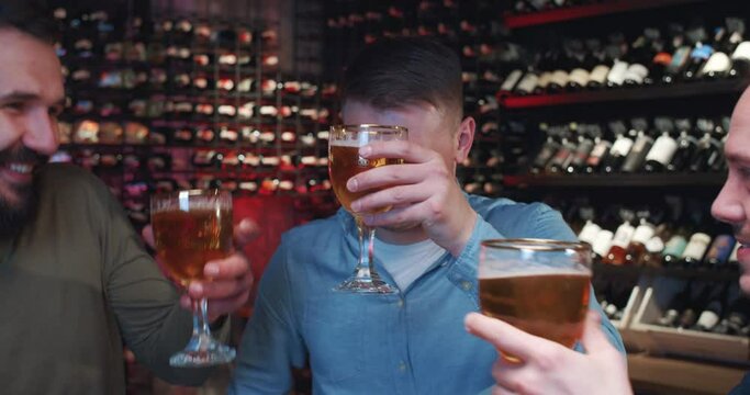 Caucasian handsome young men drinking beer in pub at night, chatting and watching sport match. Mest males friends sipping drinks and having conversation for game on sport channel. Footbal fans in bar.