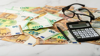 Calculator, pen and glasses on euro banknotes money background.