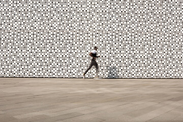 Unrecognizable sportsman running outdoors against background of contemporary building with white perforated walls, blurred motion