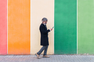 Mature businessman using mobile phone near color palette wall. Colorful background