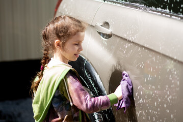 Portrait of a cute happy girl, who helps her dad wash the car outdoor. A cute girl helps her dad wash the car.