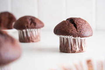 Delicious chocolate muffins in paper cups on white kitchen background. Homemade biscuit cake for breakfast