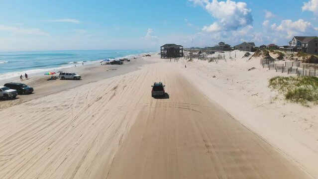 Drone following black suv on Outer Banks Corolla 4x4 beach, houses can be seen inland.