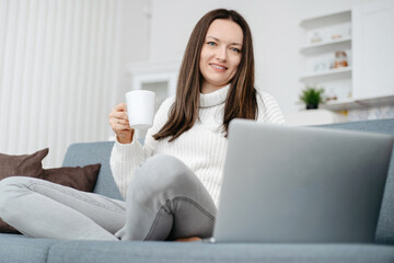 young woman sitting on the couch and using a laptop .