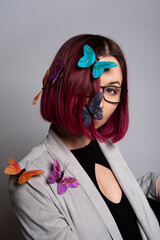 Młoda kobieta z krótkimi rubinowymi włosami z przyczepionymi kolorowymi motylami, wiosenny portret studyjny - obrazy, fototapety, plakaty