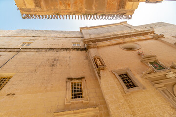 Old fortress buildings in narrow path with a clear sky above in old Malta Capital Mdina