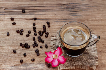 high-angle view of a cup of black americano coffee on a sackcloth rustic wooden table with a flower and a pile of organic brown coffee beans. Morning drinks concept