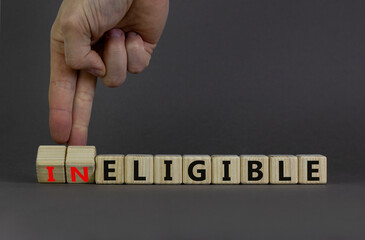 Eligible or ineligible symbol. Businessman turns wooden cubes and changes words Ineligible to Eligible. Beautiful grey table grey background. Business eligible or ineligible concept. Copy space. - obrazy, fototapety, plakaty