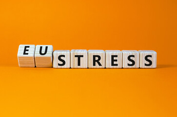Eustress or stress symbol. Turned wooden cubes and changed the concept word Eustress to Stress. Beautiful orange table orange background, copy space. Psychlogical stress or eustress concept.