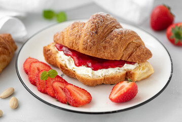 croissant with strawberry jam and cream cheese on a white plate