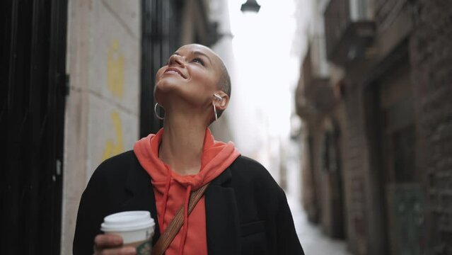 Pretty bald woman walking with cup of coffee on the street
